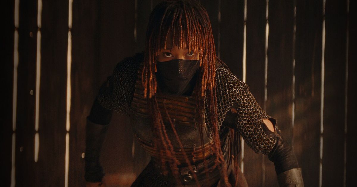 a woman with dreadlocks and a mask on her face is standing in front of a wooden wall .