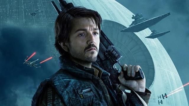 Andor Season 1 Diego Luna as Cassian Andor holding a rifle over his shoulder with ships flying behind him