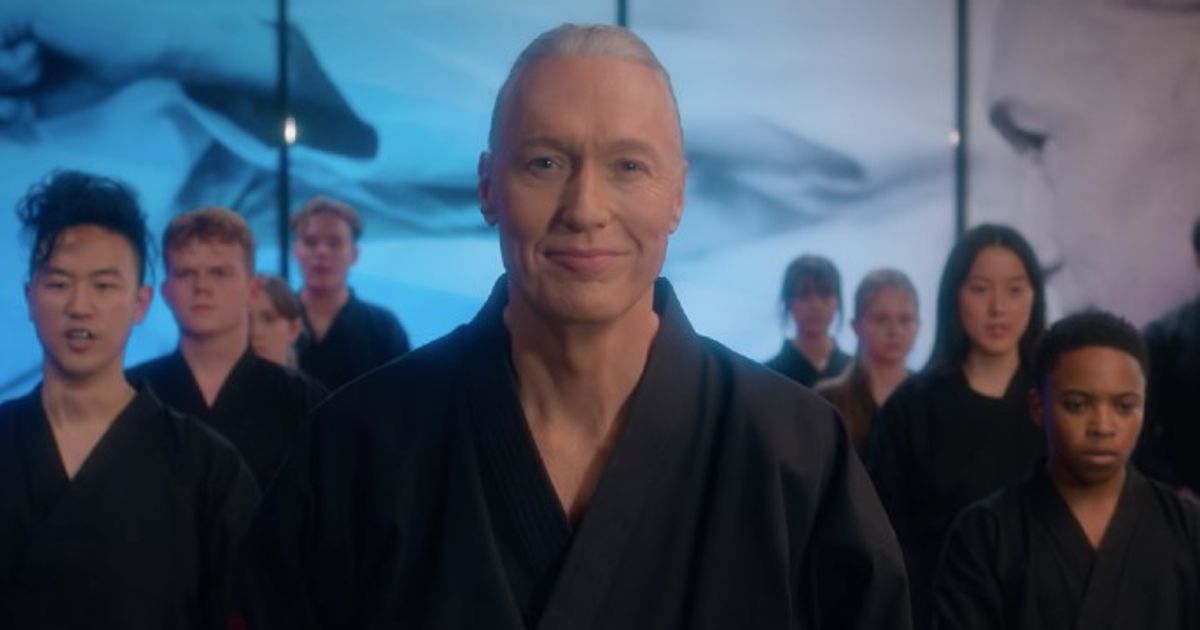 Cobra Kai Season 5 Thomas Ian Griffith as Terry Silver grins in a Cobra Kai advertisement with his students in the background